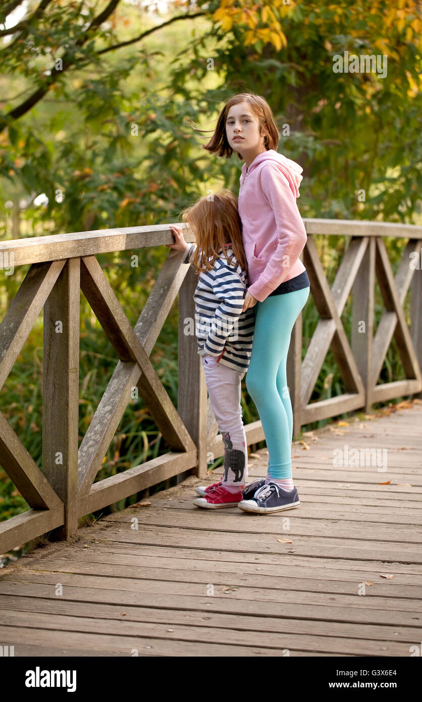 Sorelle. Una giovane ragazza tiene un occhio per la sua sorella più giovane come stanno insieme su un ponte in un parco locale Foto Stock
