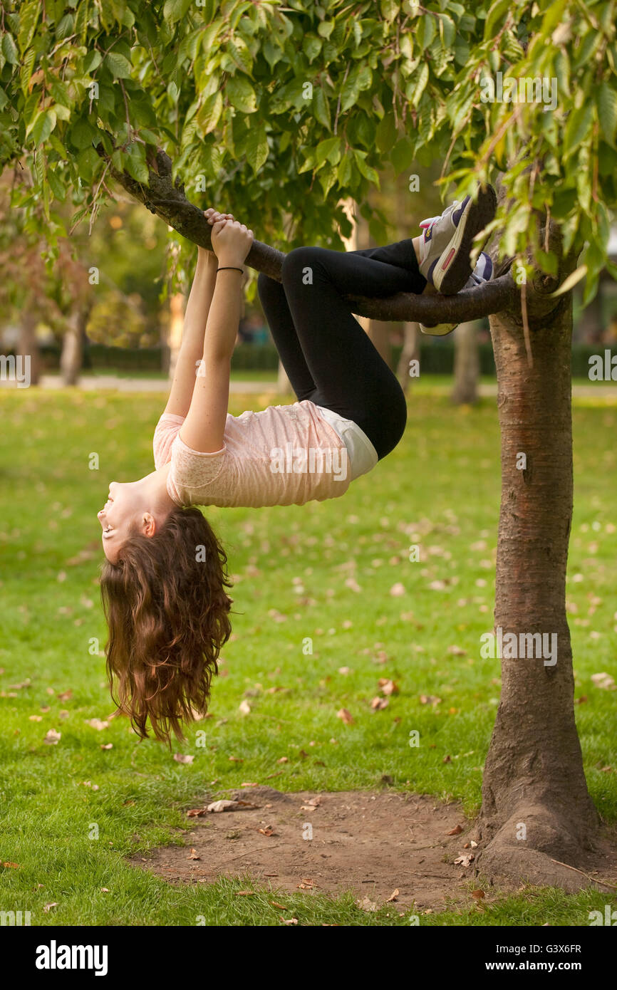 Appendere dalla struttura ad albero . Una giovane ragazza è appeso ad un ramo di un albero di piccole dimensioni. Ella è molto confortevole con essendo capovolta. Foto Stock