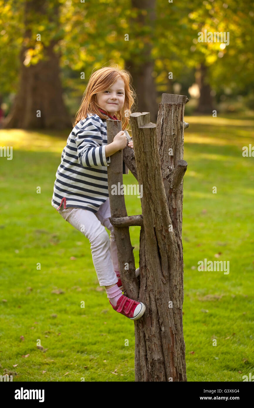Arrampicata. Una giovane ragazza felicemente si arrampica su i resti di un albero nel parco. Lo trova divertente e divertito è che essa è in grado di farlo. Foto Stock