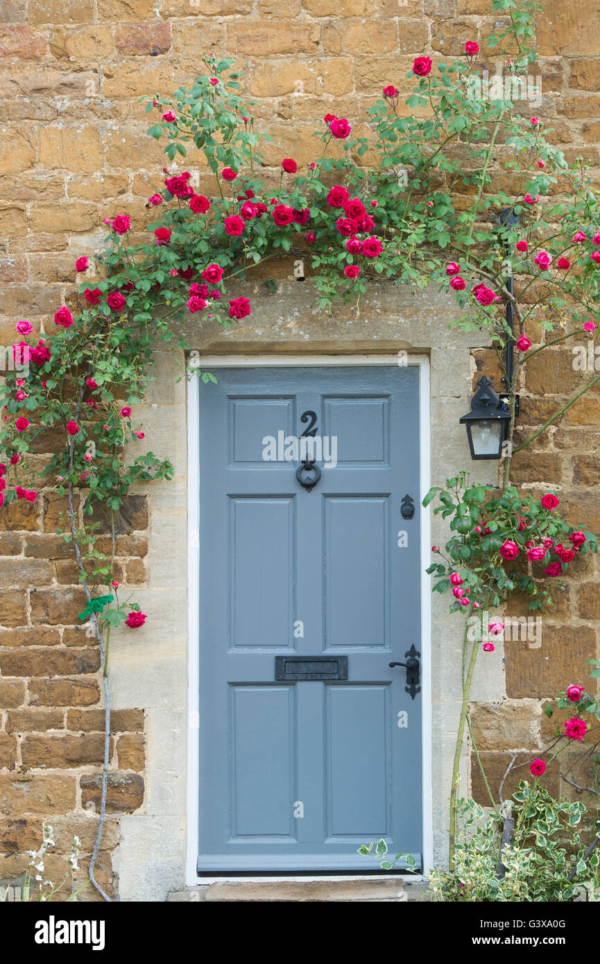 Rose rosse attorno a un legno grigio cottage in pietra porta. Adderbury, Banbury, Oxfordshire, Inghilterra Foto Stock