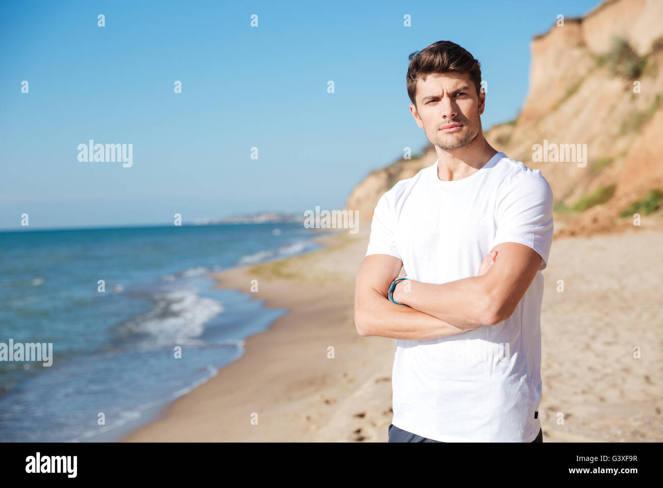 Giovane serio in piedi con le braccia incrociate sulla spiaggia Foto Stock