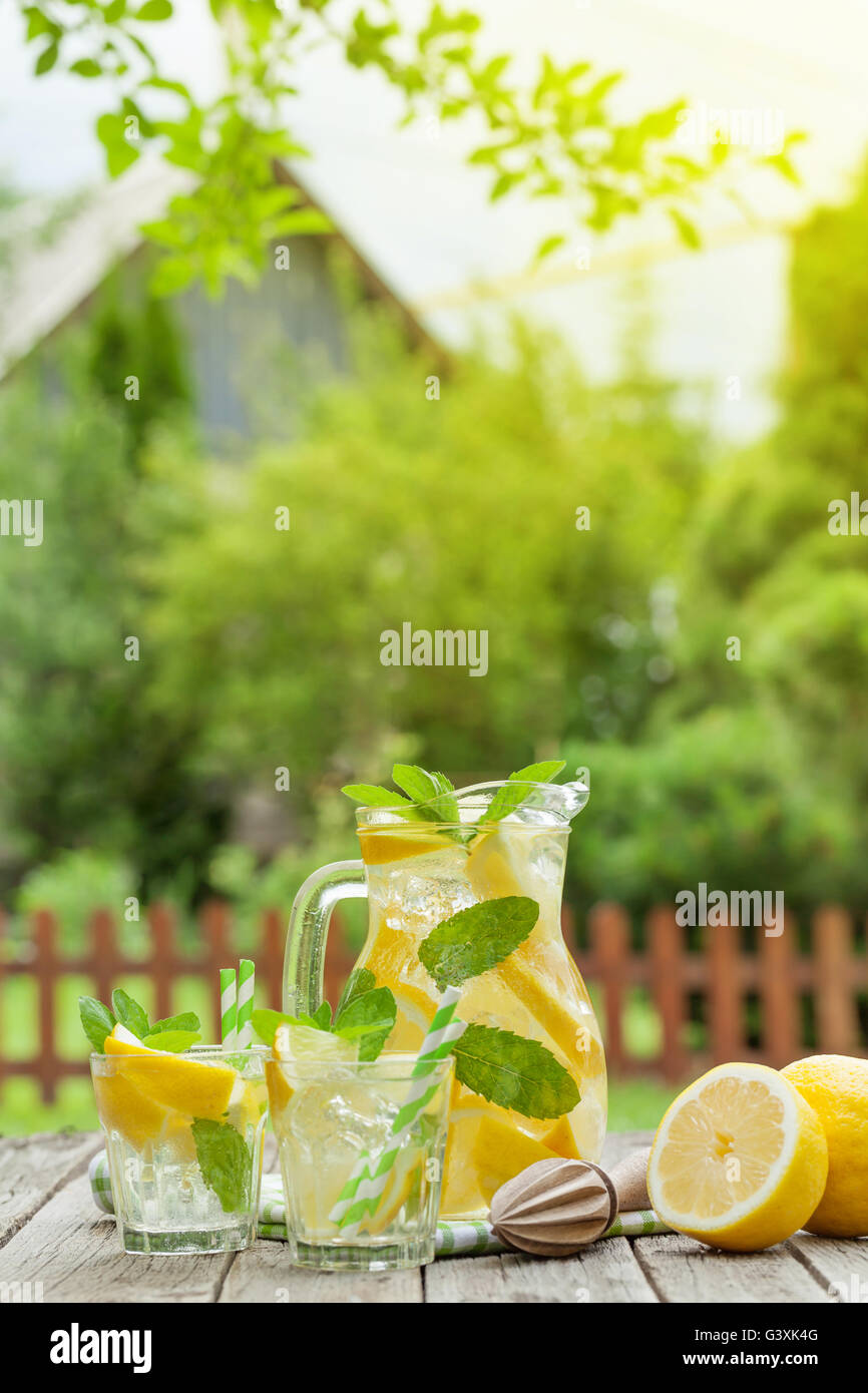 La limonata brocca e bicchieri con limone, menta e ghiaccio sul tavolo da giardino Foto Stock