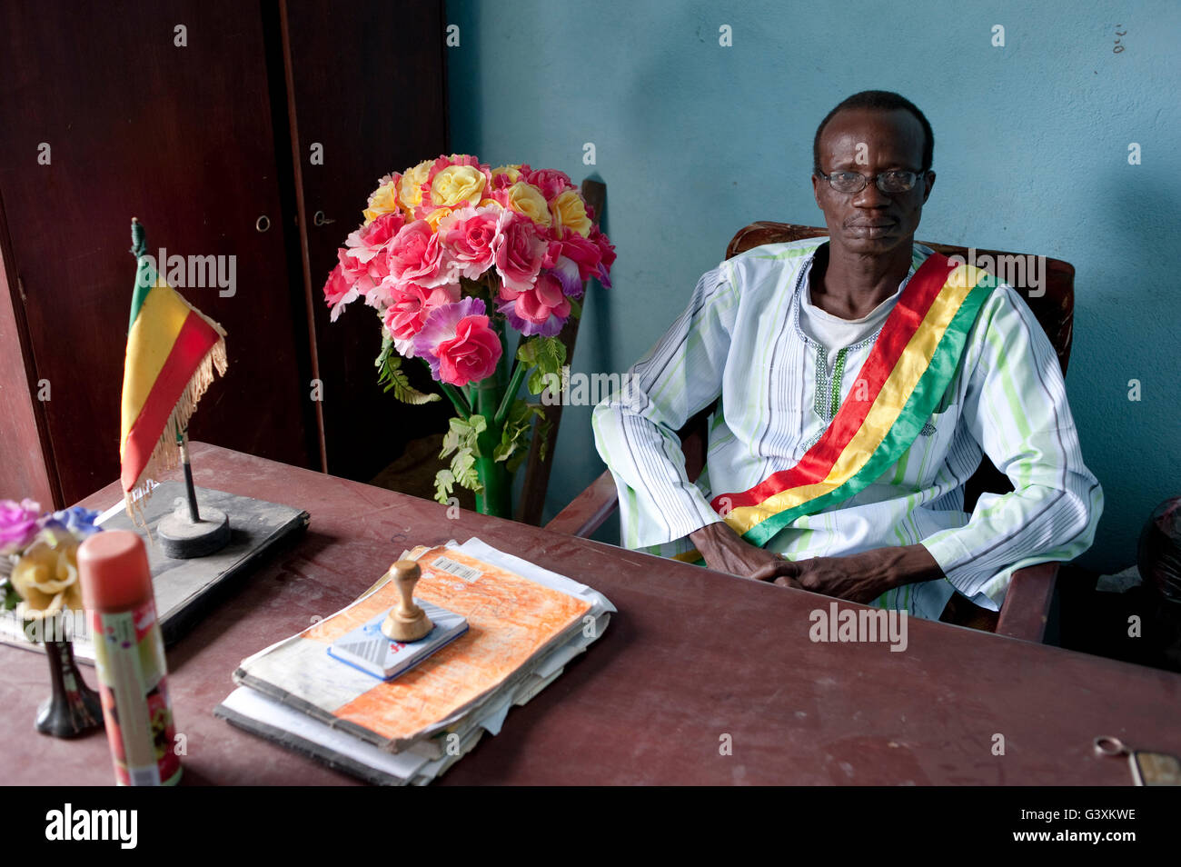 Mali, capo villaggio alla scrivania con il Mali bandiera e fiori in plastica Foto Stock