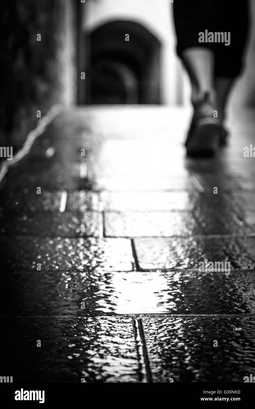 A piedi sotto la pioggia sul rustico in pietra pavimento in Italia in bianco e nero Foto Stock