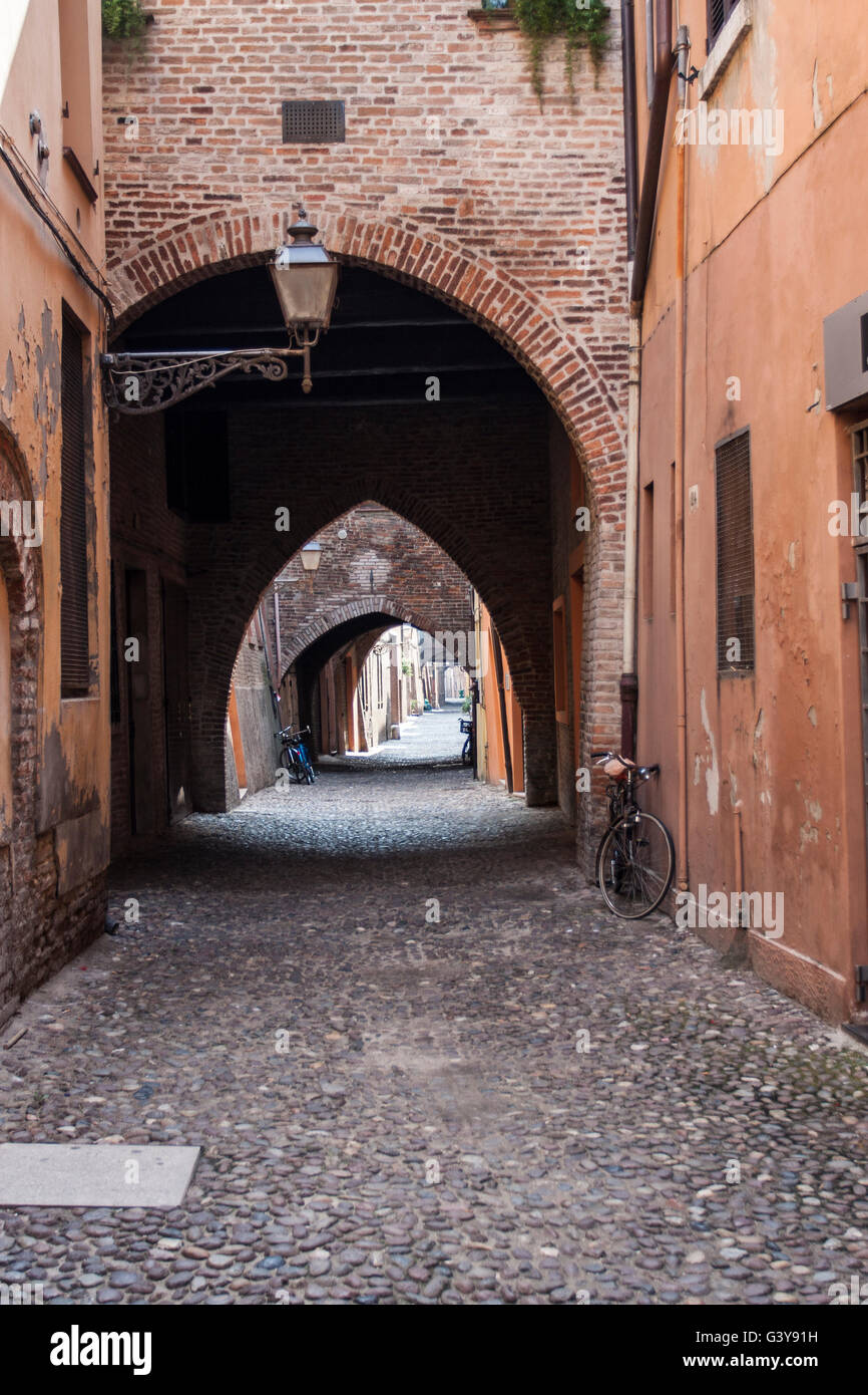 Vista del vicolo stretto nella vecchia città di Ferrara con arco e pavimentazione in ciottoli. Foto Stock
