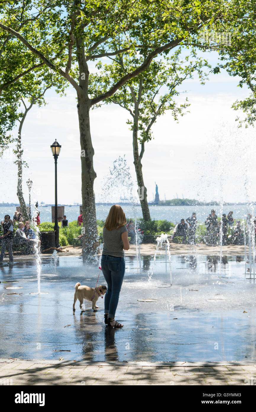 Donna che cammina il suo cane Pug in acqua delle fontane per aiutare a farlo raffreddare in un caldo giorno d'estate a Battery Park, New York Foto Stock