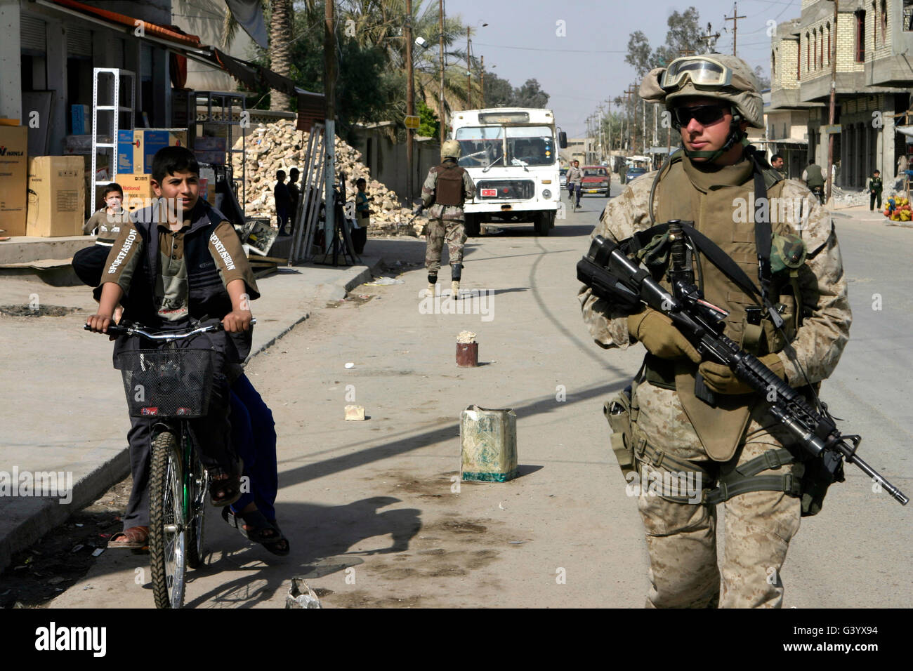 Una macchina gunner cammina al fianco di un ragazzo iracheno su una bicicletta. Foto Stock