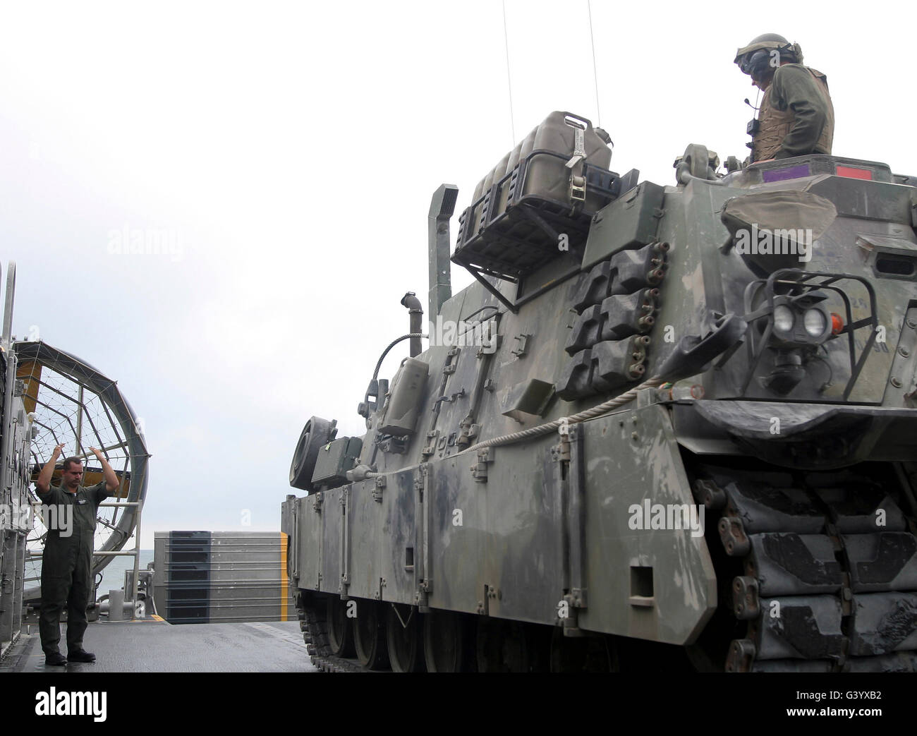 Una Landing Craft, Air-Cushioned loadmaster segnala l'equipaggio di un M88A2 Hercules veicolo di recupero. Foto Stock