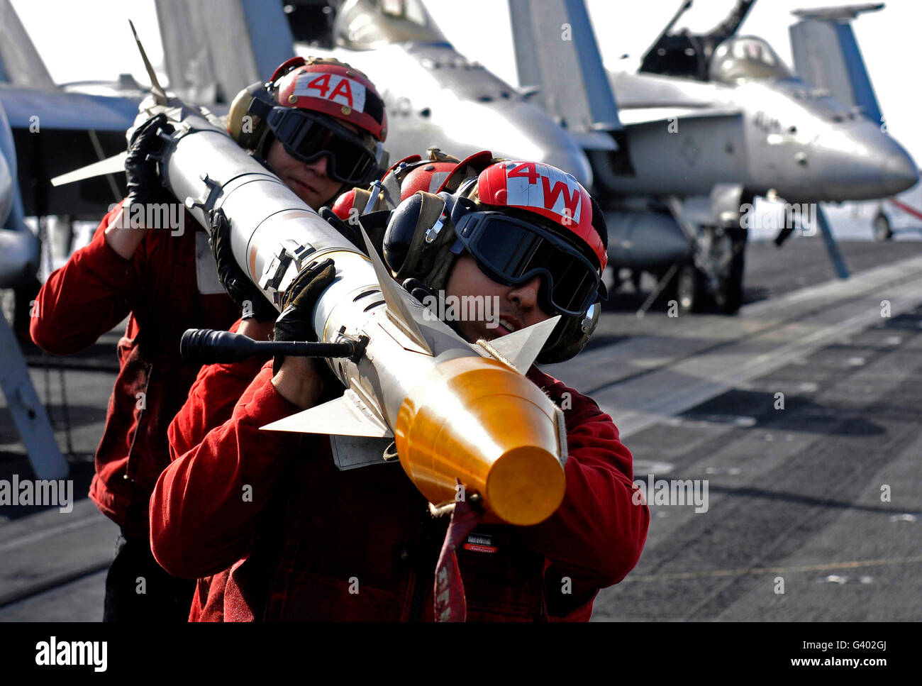 Aviation Ordnancemen trasportare un missile air-air sul ponte di volo. Foto Stock