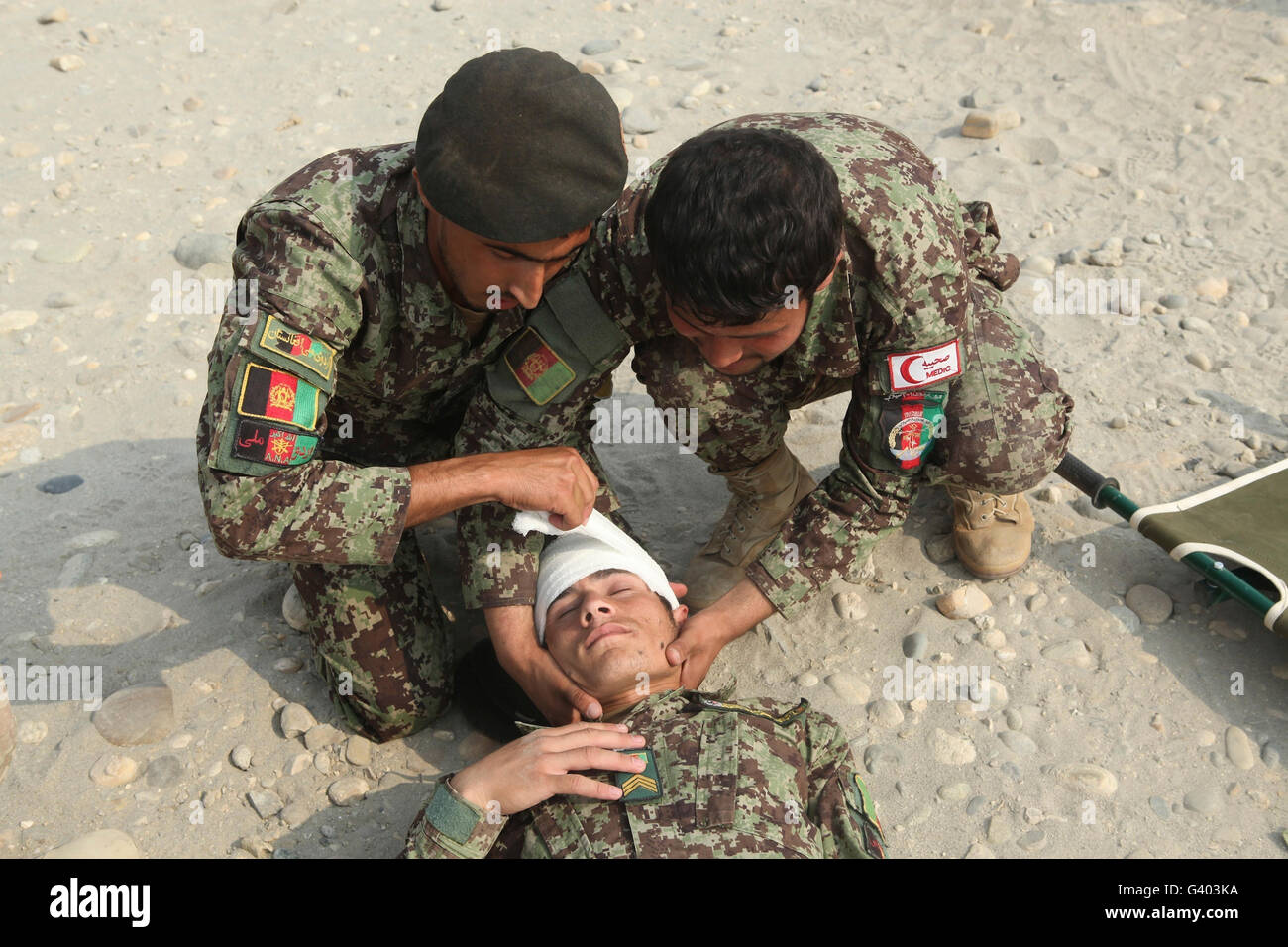 Esercito Nazionale Afghano soldati misero un bendaggio di testa su un compagno soldato. Foto Stock