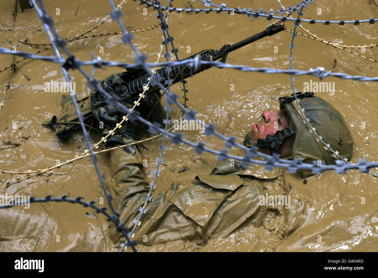Un soldato crawl posteriore attraverso una fossa rivestita in filo di concertina. Foto Stock