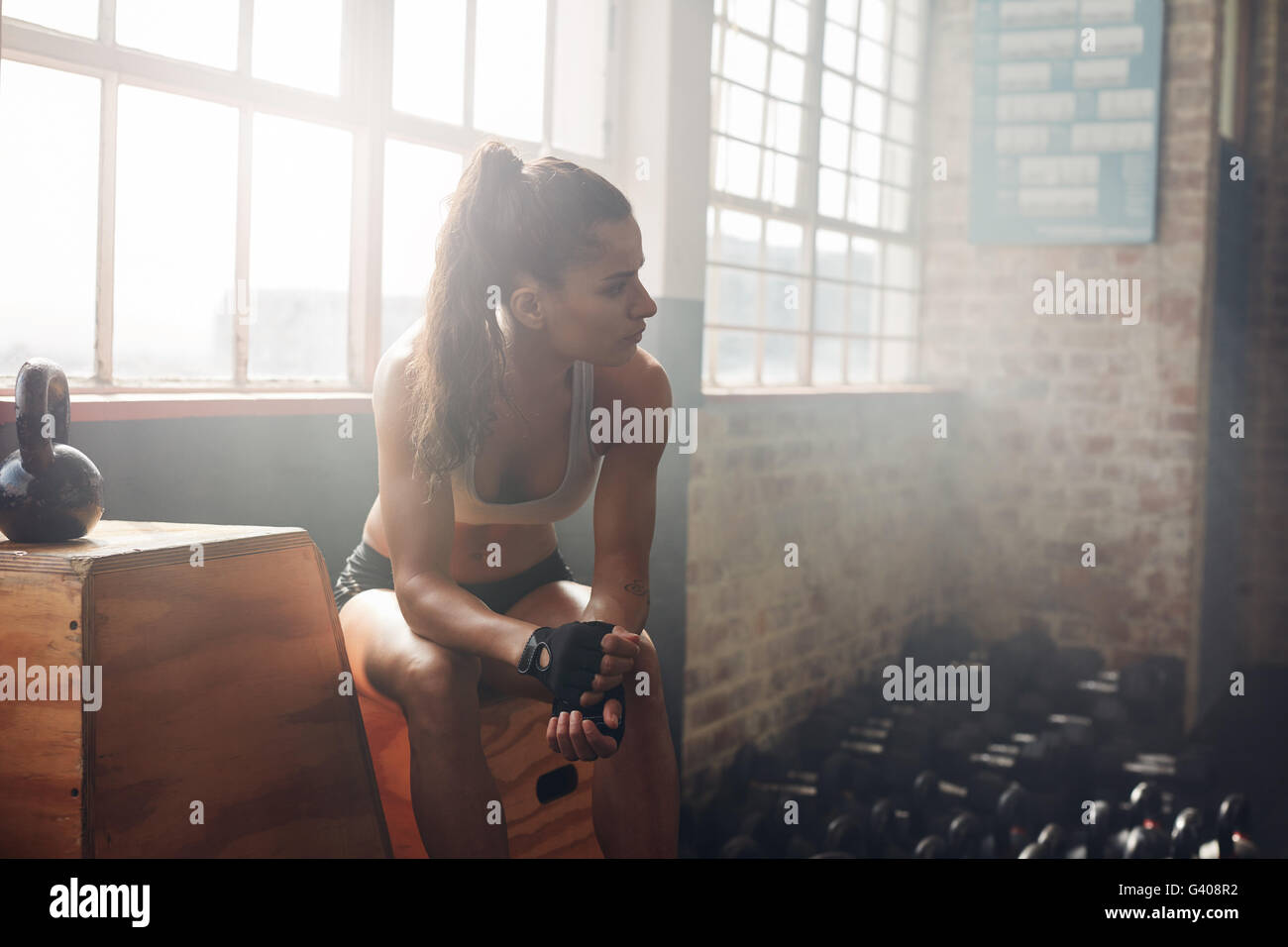 Piscina colpo di sano giovane donna rilassante sulla casella nella palestra e guardando lontano. Atleta femminile donna avente un riposo dopo esercizio fisico. Foto Stock