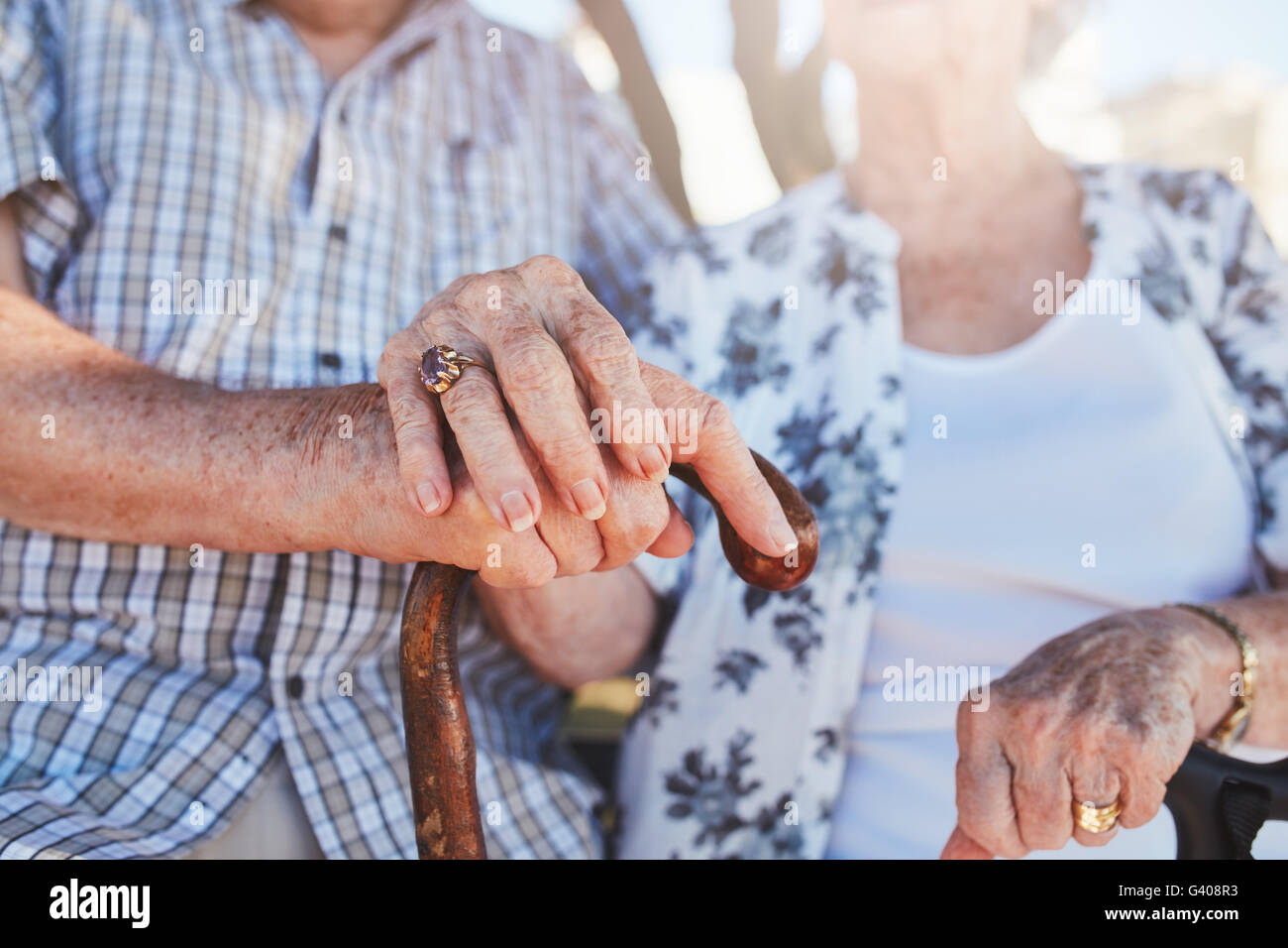 Ritagliato colpo di coppia senior holding hands seduti insieme. Focus su mani sul bastone. Foto Stock