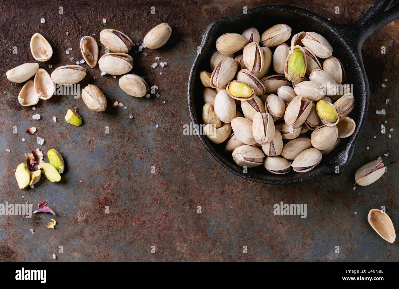 Salate pistacchi tostati di noci con guscio e sale in in nero piccolo cast-padella di ferro su un vecchio ferro arrugginito sfondo a trama. A Foto Stock