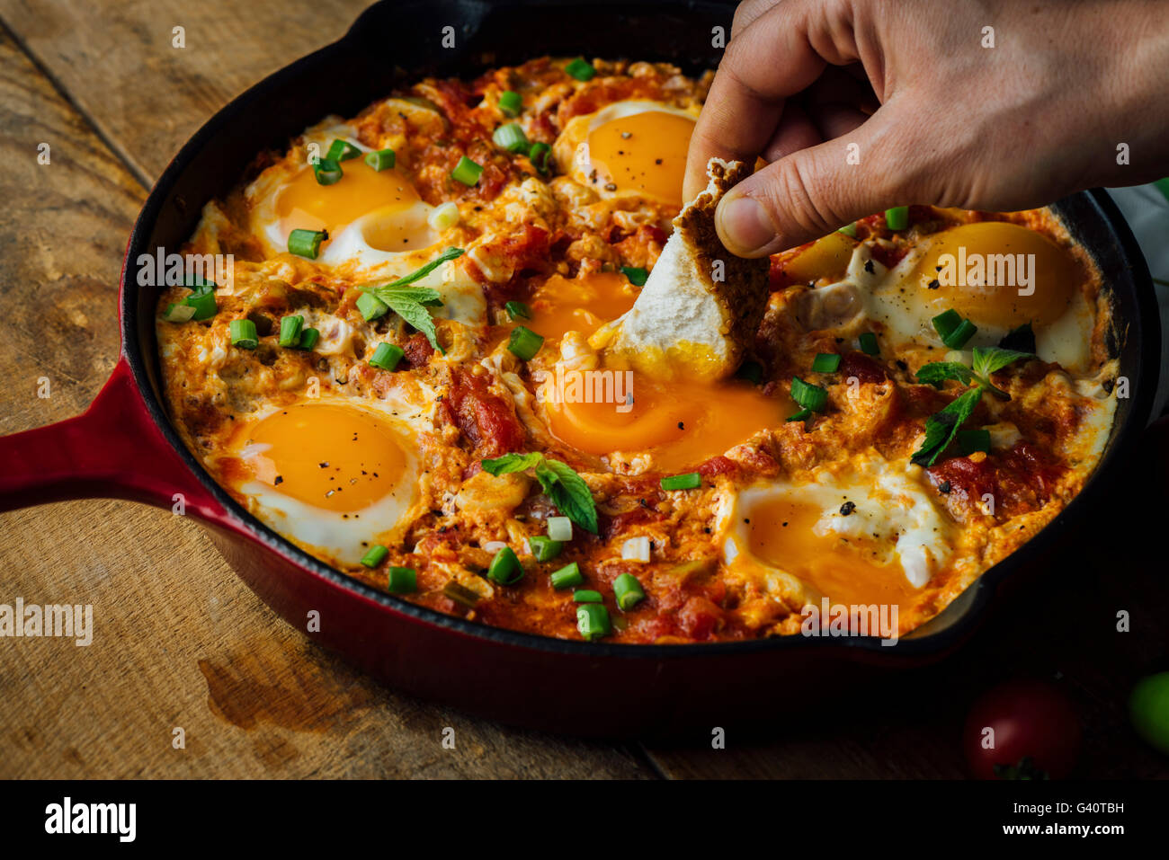 Immersione di un tradizionale pane turco chiamato simit in un uovo piatto fatto con uova, pomodori e peperoni verdi chiamato menemen o s Foto Stock