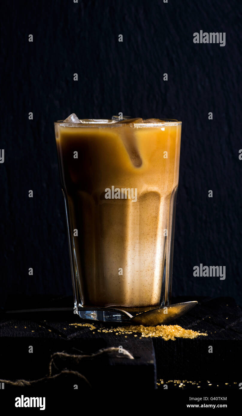 Caffè ghiacciato con il latte in un bicchiere alto, sfondo nero, il fuoco selettivo Foto Stock