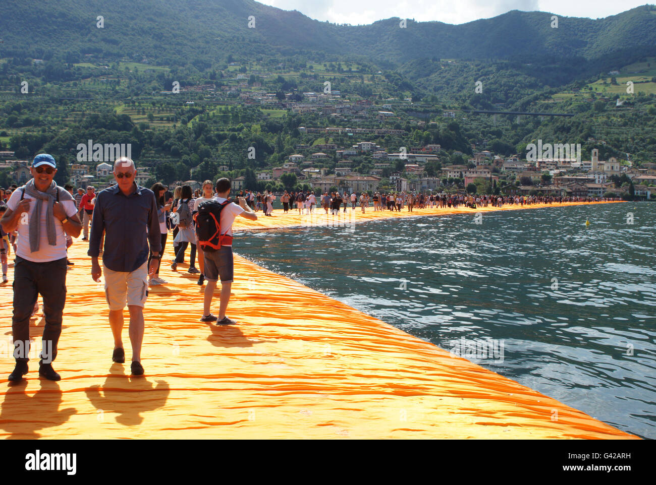 Sulzano, Italia. Il 18 giugno, 2016. I visitatori a piedi attraverso pontili galleggianti rivestito in tessuto di colore arancione come parte del progetto "i pontili galleggianti' di Christo sul Lago d'Iseo lago, che corre dall'isola Monte Isola a Sulzano, Italia, 18 giugno 2016. Christo aveva un molo costruito da Paratico verso l' isola di Pesciera e coperto il molo e la riva in tessuto. Il progetto artistico di Christo sulla parte settentrionale del lago italiano apre il 18 giugno e continua fino al 03 luglio 2016. Foto: Carola Frentzen/dpa/Alamy Live News Foto Stock