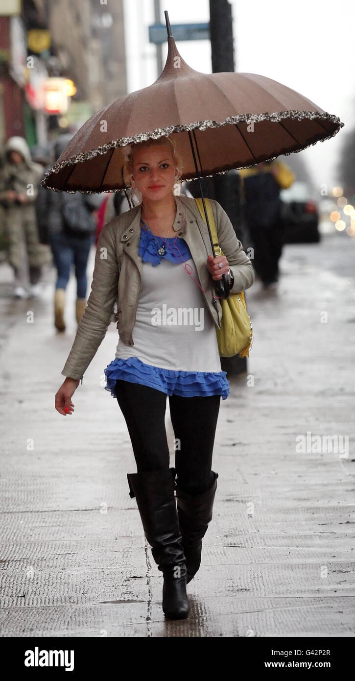 Un membro del pubblico prende copertura sotto un ombrello a Glasgow, Scozia, mentre il tempo severo continua. Foto Stock