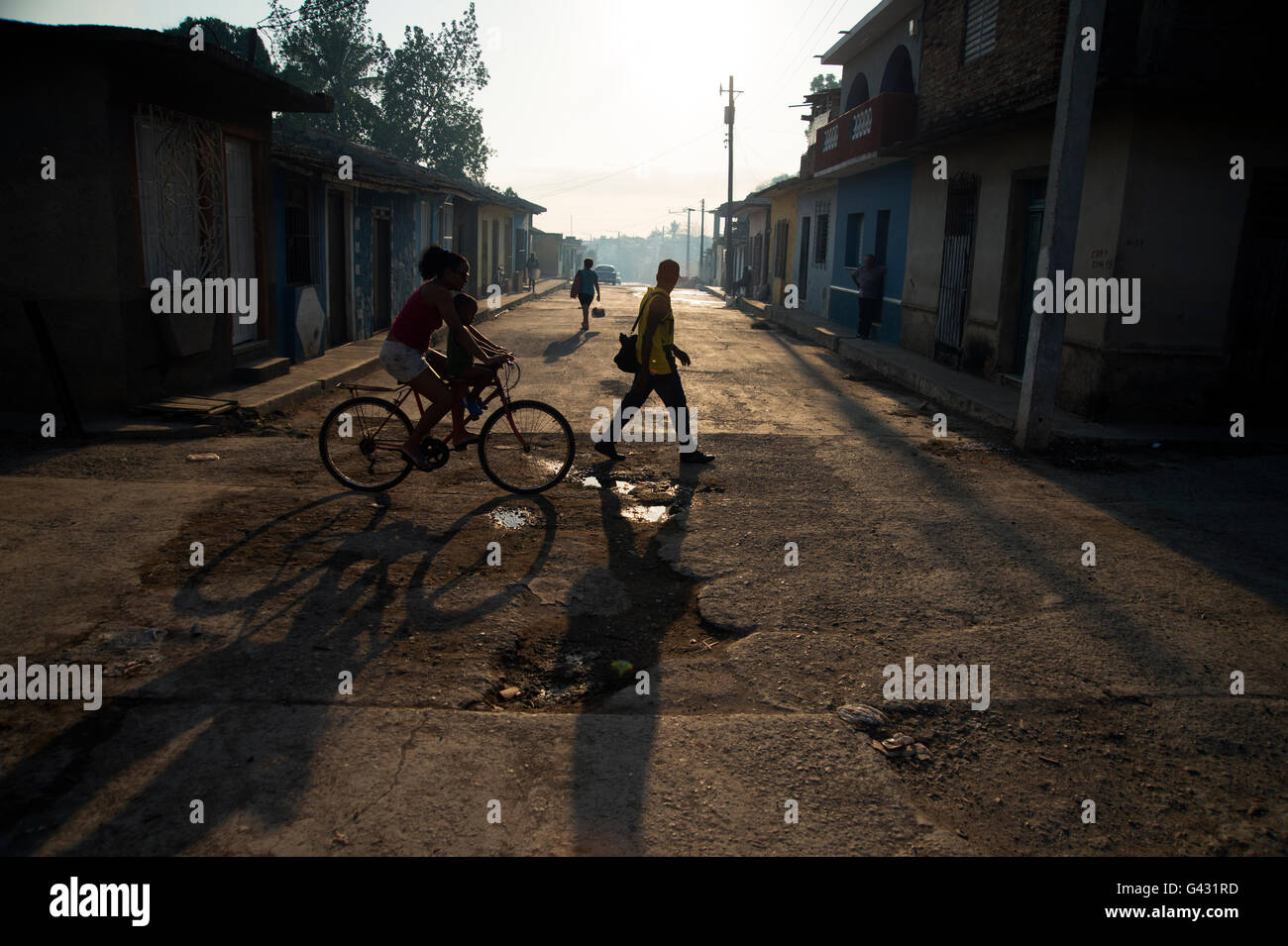 Sagome di una donna su una bicicletta e la gente che camminava per le strade di Trinidad Cuba come il sole tramonta Foto Stock