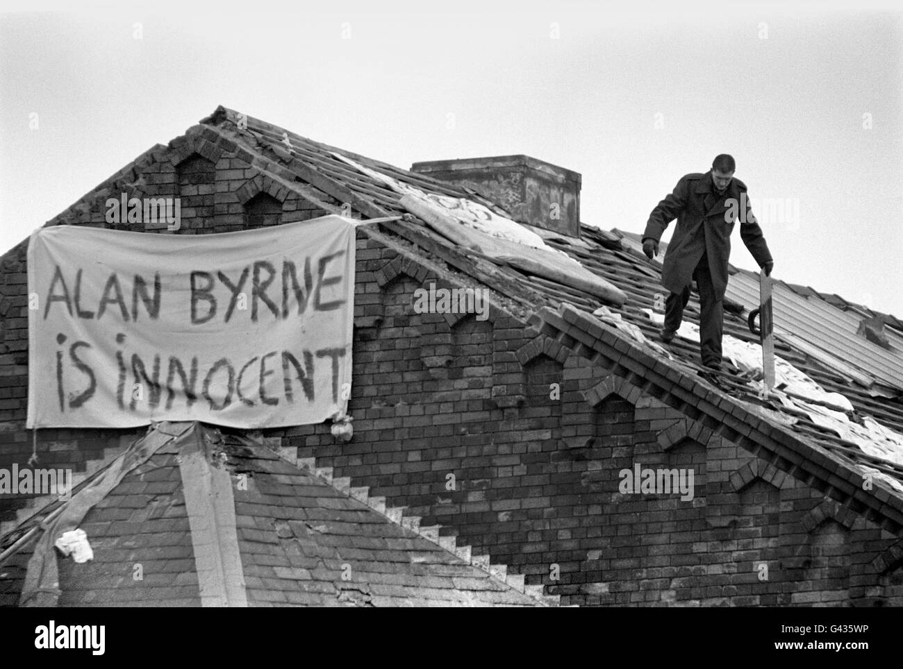Un prigioniero solo raccoglie uno scudo di rivolta sul tetto della prigione di Strangeways a Manchester, come un banner con lo slogan "Alan Byrne is Innocent", pende dal muro Foto Stock