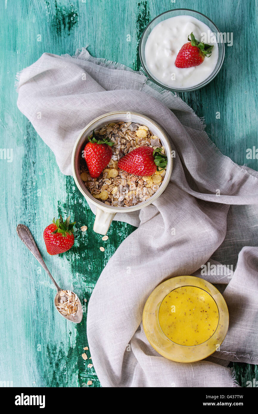 Ingredienti per una sana prima colazione. Yogurt, ciotola di muesli con fragole e bicchiere di mango smoothie con semi di chia su bianco Foto Stock