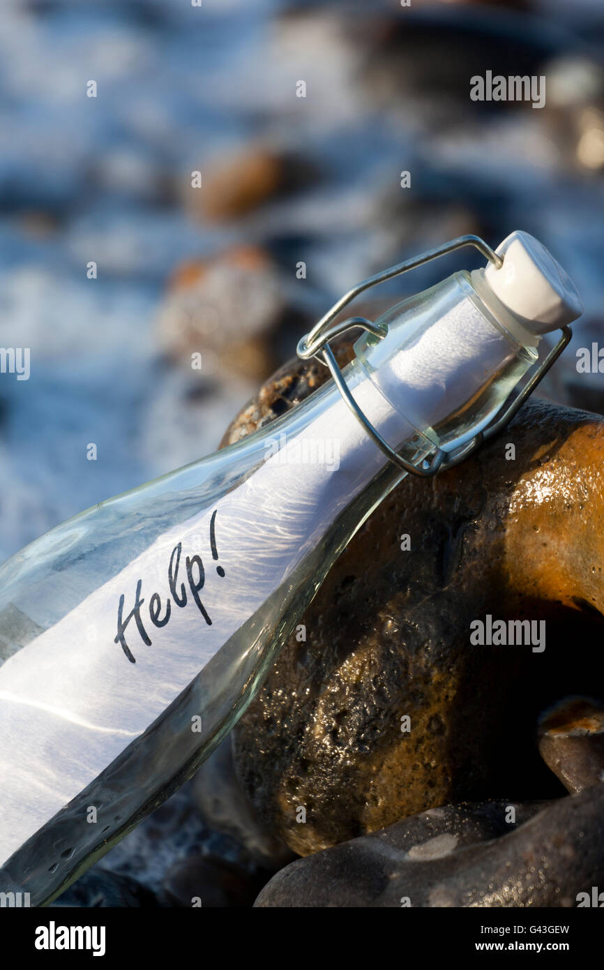 Un messaggio di 'Help' in una bottiglia di vetro su una spiaggia Foto Stock