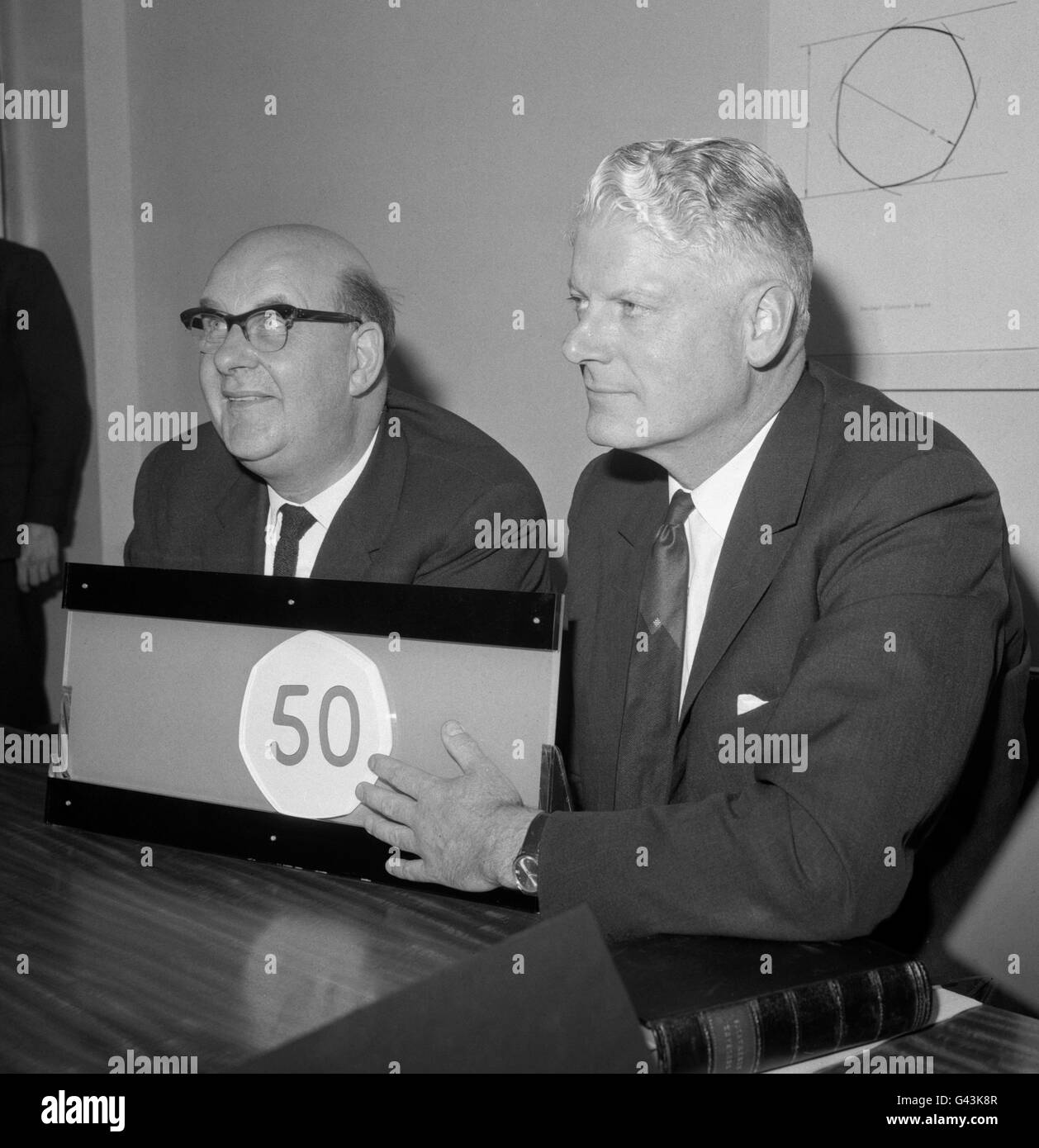 Lord Fiske (sinistra) Presidente del Decimal Currency Board e Hugh Conway, direttore della Rolls Royce Ltd, E un membro del Machine Committee del consiglio di amministrazione, che dimostra un ingrandimento del modello plastico della nuova moneta da 50 pence nei corridori di un distributore automatico presso la sede del consiglio di amministrazione in Northumberland Avenue, Londra. Foto Stock