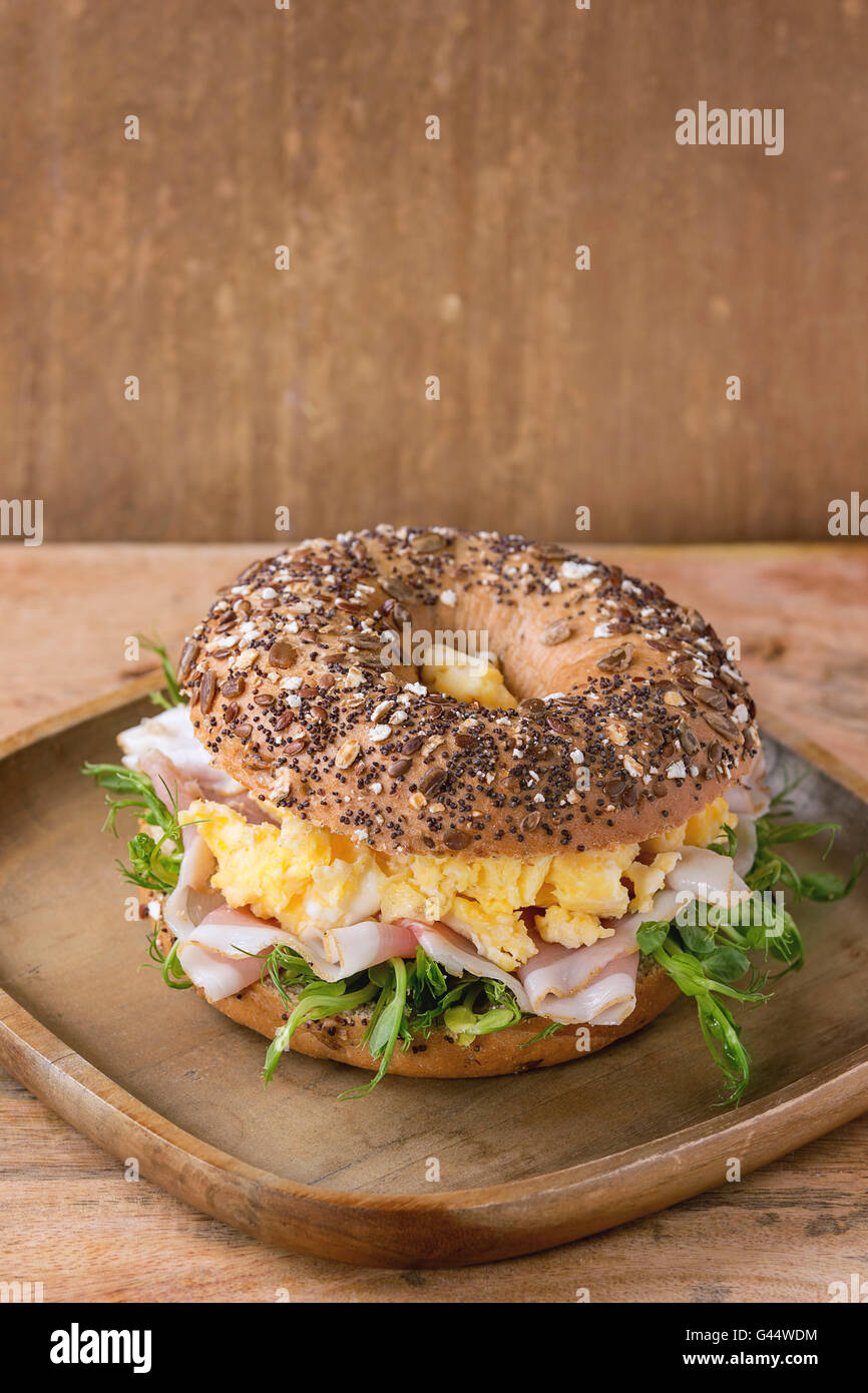 Cospargere con semi di grano intero ciambelle di pane con uova strapazzate, germoglio di piselli e prosciutto crudo sul piatto di legno su legno backgrou testurizzata Foto Stock