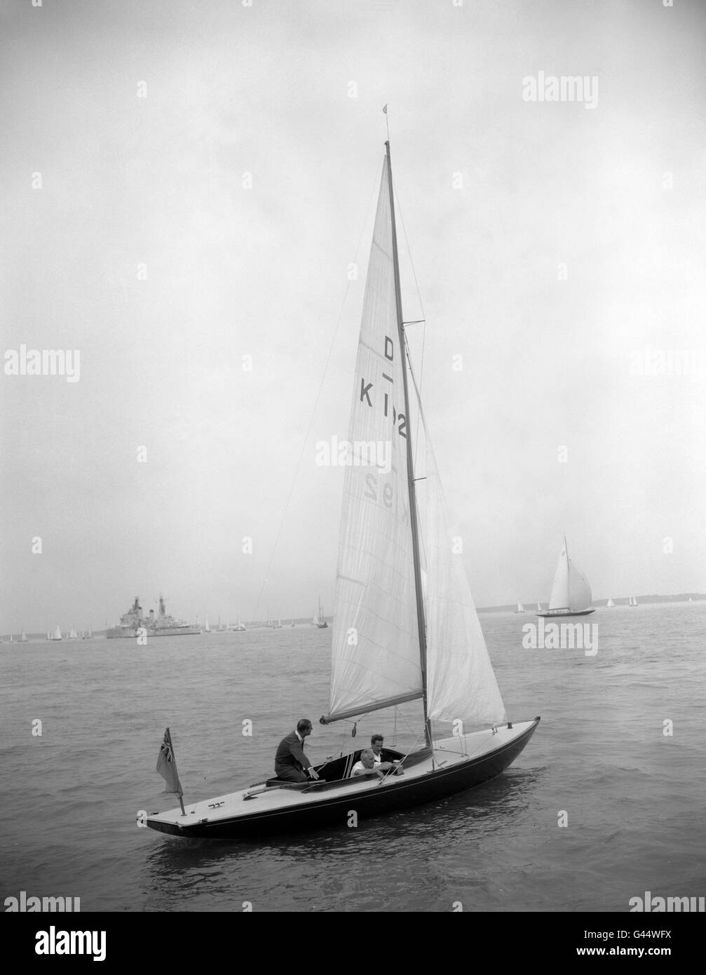 Il Duca di Edimburgo (a sinistra) si inclina in avanti per afferrare il timone dello yacht 'Bluebotole', che possiede insieme alla Regina, il quarto giorno della settimana della Regata dei Cowes. Il Duke è stato accompagnato da Uffa Fox, esperto di corse di yacht. Foto Stock