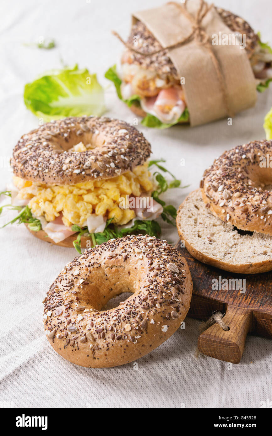 Vuoto e personale grano intero ciambelle di pane con uova strapazzate, pisello germoglio, cipolle fritte e prosciutto crudo, rendendo sulla biancheria da letto bianca tabella Foto Stock