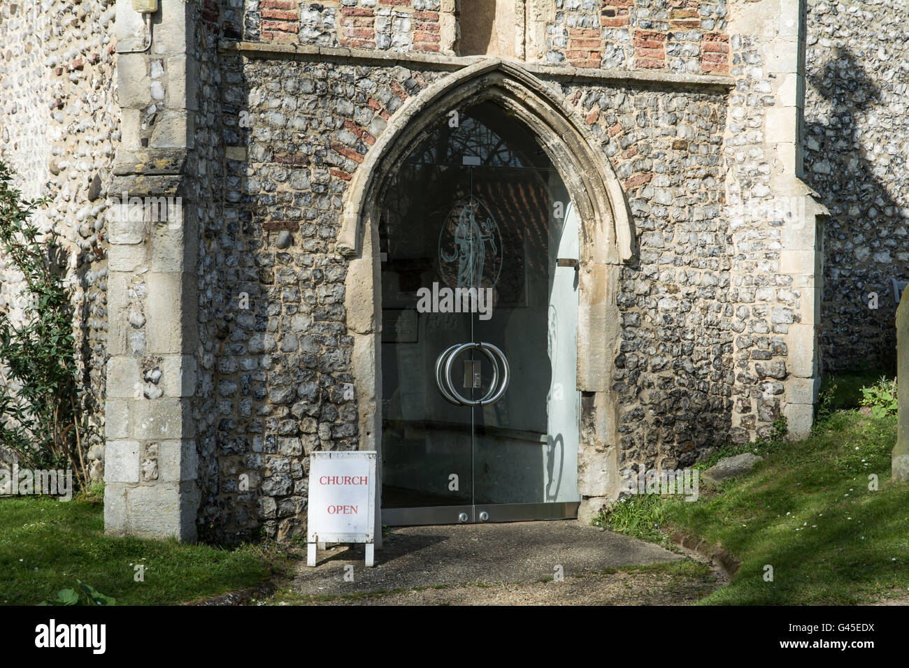 Una moderna porta in vetro su una vecchia chiesa. Prese a Weybourne Chiesa, Norfolk. Foto Stock