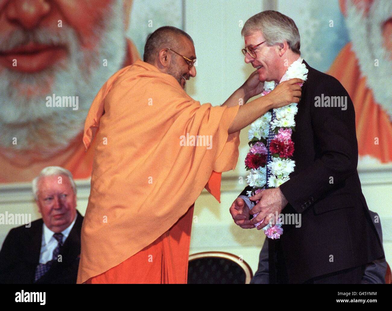 Il primo ministro John Major è presentato con una ghirlanda di fiori da Atmaswarupdas (il prete capo) come l'ex Premier Sir Edward Heath guarda questa sera (Domenica). Gli uomini politici si sono ritrovati a condividere una barzelletta sulla moneta unica europea durante i loro discorsi ad oltre 4,000 asiatici e indiani presso il tempio indù di recente apertura a Neasden, nel nord di Londra. Foto di Fiona Hanson/PA/Pool. VEDERE LA STORIA PA POLITICA MAGGIORE Foto Stock