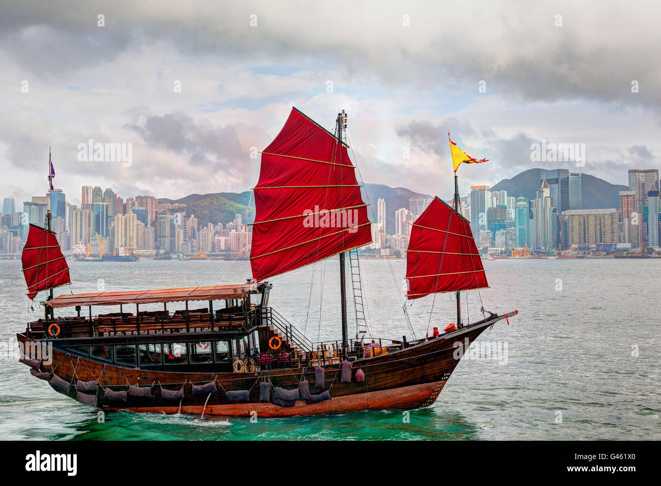 Rendering HDR di una tipica giunca Cinese nave con vele rosso sul Victoria Harbour in Tsim Sha Tsui Hong Kong. I riflessi color smeraldo Foto Stock