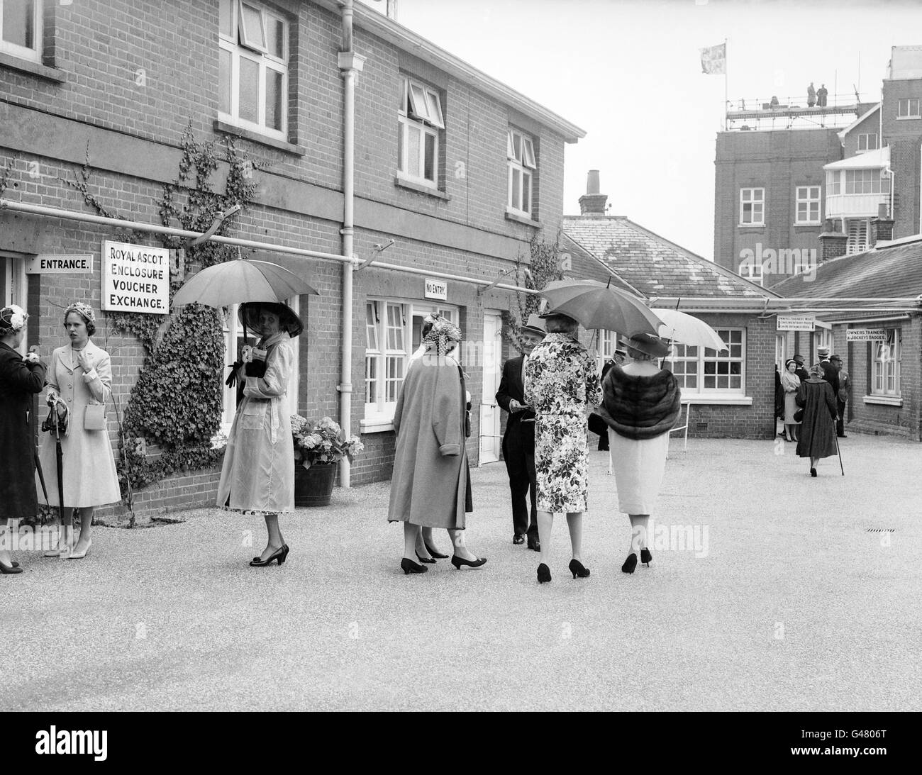 Corse ippiche - Ascot reale - Ascot Racecourse. Completa di ombrelloni in su, le donne aspettano fuori dall'entrata al recinto di Ascot Foto Stock