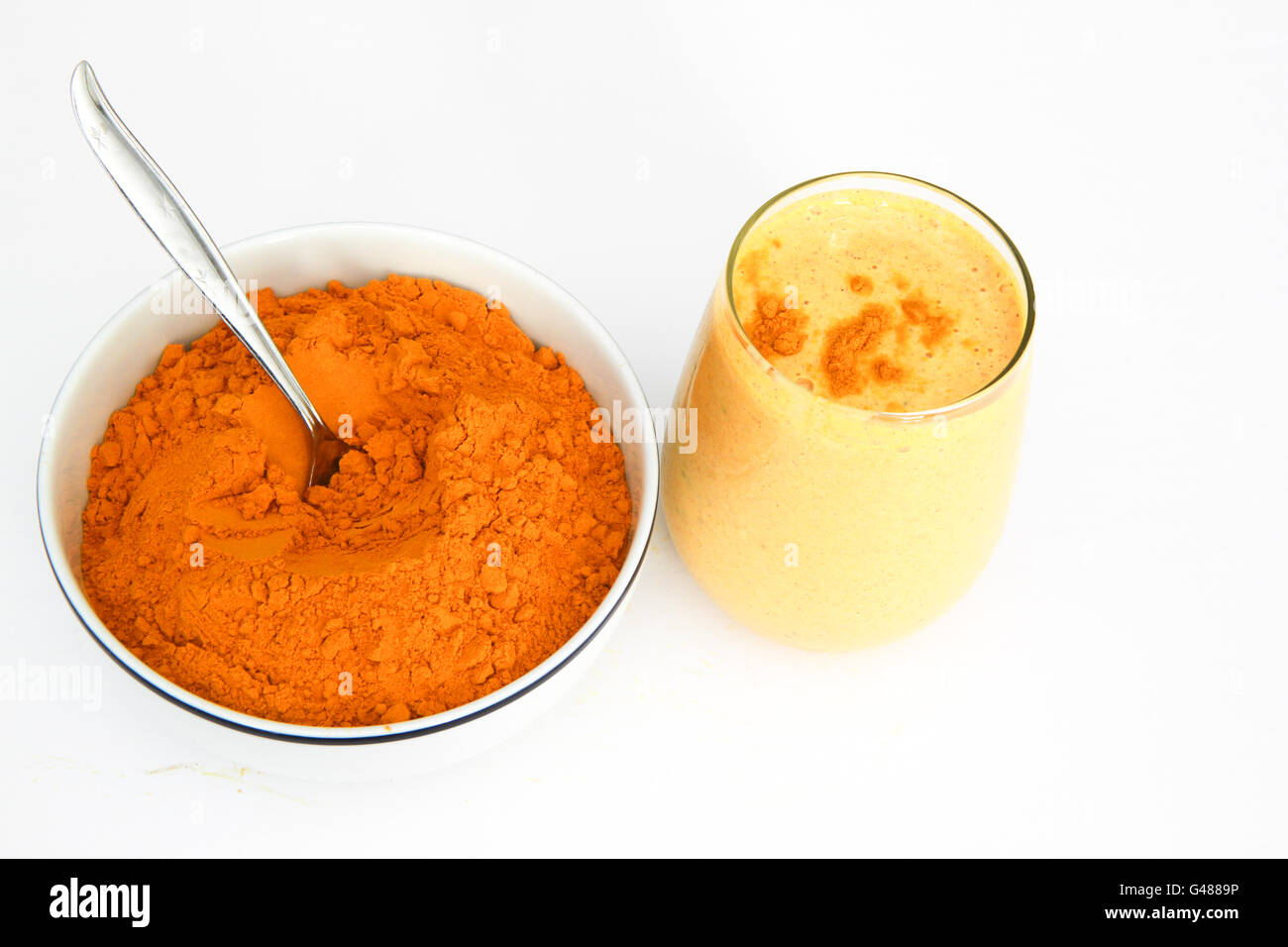 Curcuma e zenzero frullato frullato in vetro stemless con coppa di polvere di curcuma accanto al vetro, isolato su bianco Foto Stock