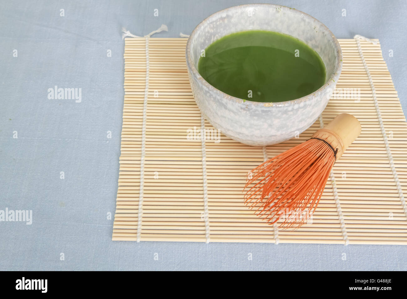 Tè verde Matcha in pietra abbeveratoio sul cartellone di bambù con frusta in legno nella parte anteriore del recipiente su luce blu tovaglia. Foto Stock