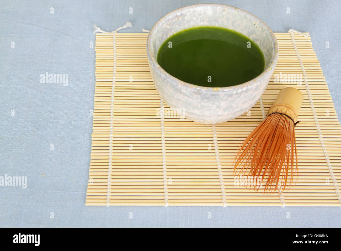 Tè verde Matcha in pietra abbeveratoio sul cartellone di bambù con frusta in legno nella parte anteriore del recipiente su luce blu tovaglia. Foto Stock