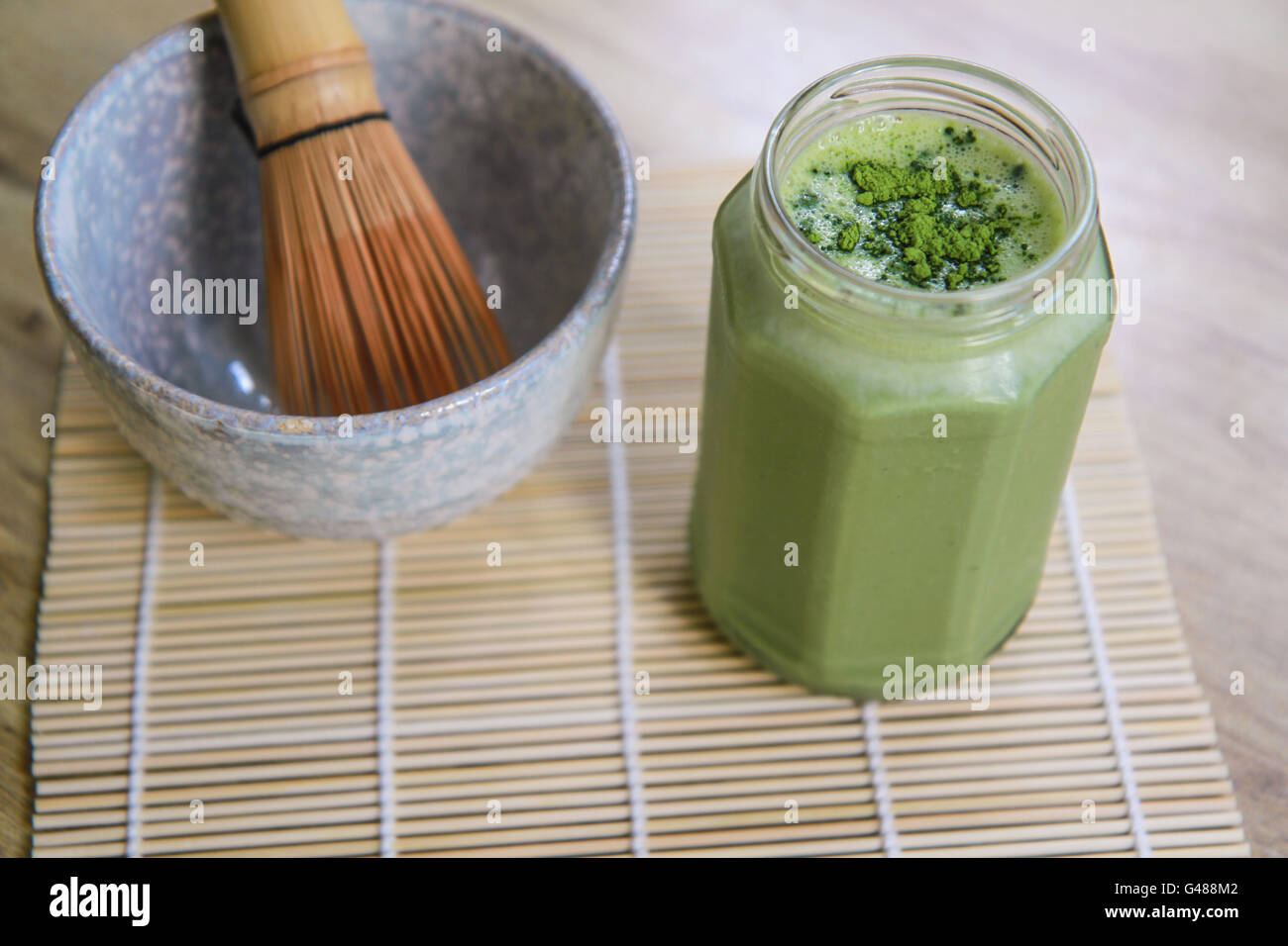 Tè verde Matcha smoothie in un barattolo di vetro con la pietra di ciotola e mescolare con una frusta di legno sul tappetino di bambù sulla tabella precedente angolo di visione Foto Stock Tè verde Matcha smoothie in un barattolo di vetro con la pietra di ciotola e mescolare con una frusta di legno sul tappetino di bambù sulla tabella precedente angolo di visione Foto Stock