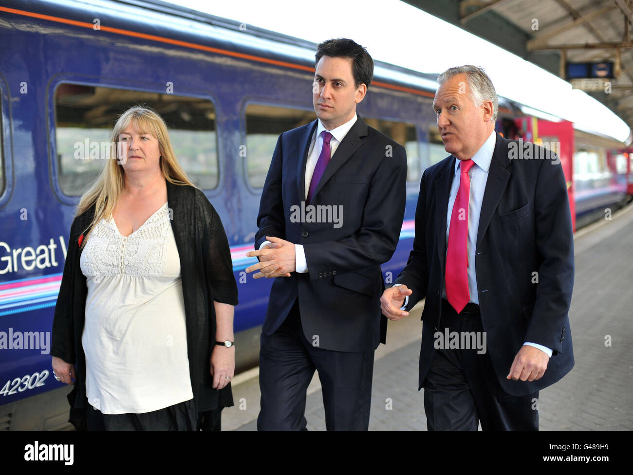 Il leader del Labor Party ed Miliband è accompagnato dal laburista MP per Neath Peter Hain e dal candidato laburista Julie James (a sinistra) dopo l'arrivo alla stazione ferroviaria di Swansea durante una visita al Galles meridionale. Foto Stock