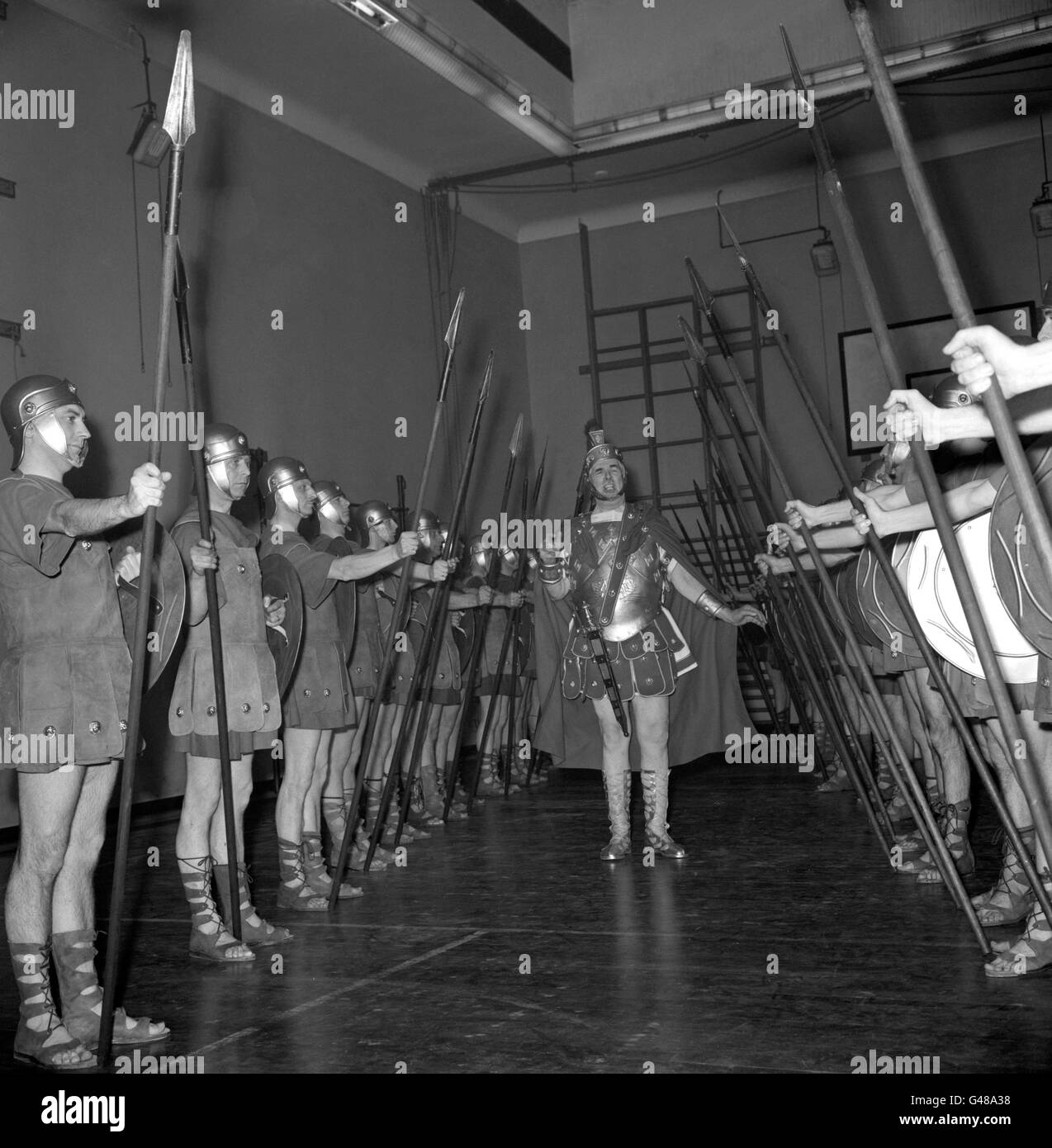 L'ex Sergente Regimental Major Ronald Brittain, centro, mette un gruppo di reclute 'Roman' attraverso i loro movimenti di perforazione alla Bedford School, Holborn Boys Club, Londra. Britain sta usando la sua famosa voce forte per addestrare 32 ex Guardmen che compariranno nell'uniforme dei centurioni romani alla premiere di beneficenza del film 'Sparacus'. Foto Stock