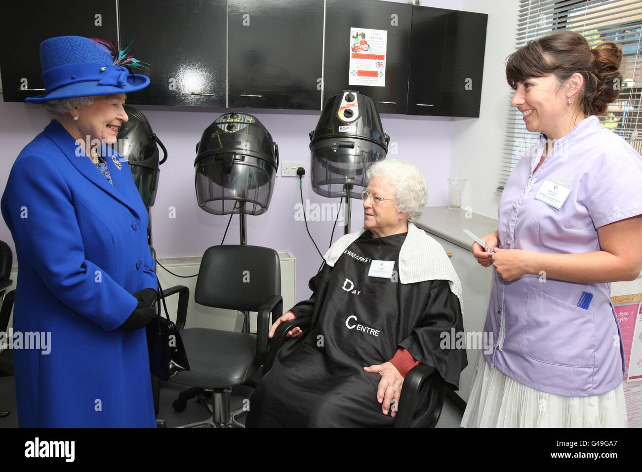 La regina Elisabetta II parla con vera Smith, da Stetchworth, e con il parrucchiere Claire Tombes, da Newmarket, Suffolk, durante una visita ai parrucchieri interni al Newmarket Day Center in città. Foto Stock