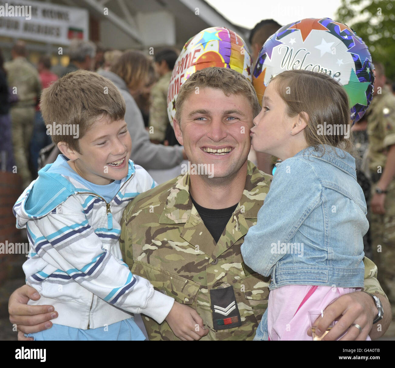 I gemelli Thomas e Hope McGinlay (a destra), di otto anni, baciano il loro padre, il caporale Michael McGinlay, mentre torna nel Regno Unito con lo Squadron finale del 2° Regiment Royal Tank (2 RTR), con sede a Tidworth, Wiltshire, dopo un tour di sei mesi di successo in Afghanistan. Foto Stock