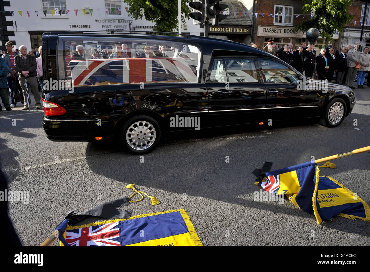 La bandiera dell'Unione ha bevuto la bara del funzionario di garanzia di classe 2 Graham Bean, che è morto il 3 maggio dopo essere stato improvvisamente ammalato durante la mountain bike, si muove lentamente oltre gli standard abbassati della Legione Britannica reale, come il serveman di 54 anni, Che ha servito con i volontari regimentali del 73, passa attraverso la High Street della città di Wootton Bassett nel Wiltshire, mentre il corpo di Graham viene rimpatriato nel Regno Unito. Foto Stock