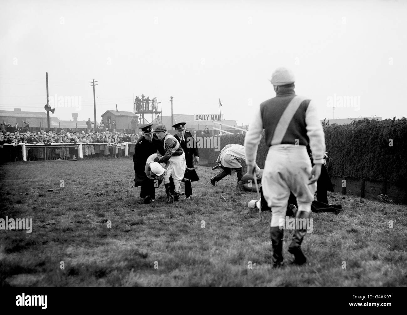 Il jockey Johnny Lehane, che è caduto al Brook di Becher il primo turno, presta una mano d'aiuto agli uomini dell'ambulanza che trasportano un jockey che è caduto alla stessa recinzione. Foto Stock