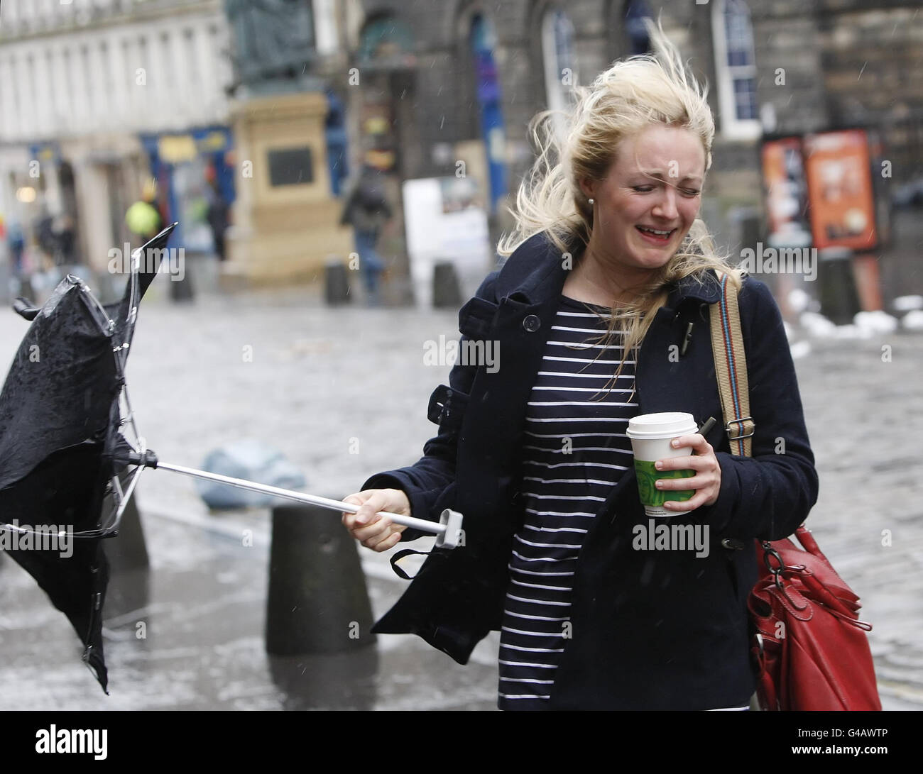 Una donna combatte con un ombrello in condizioni ventose sul Royal Mile di Edimburgo, poiché le galee gravi colpiscono la parte settentrionale del Regno Unito. Foto Stock