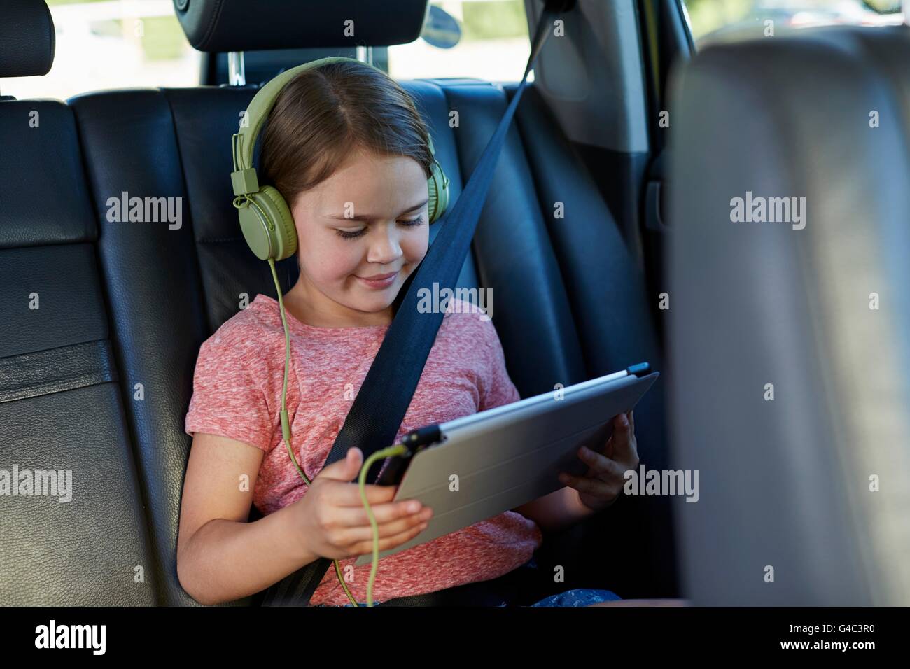 Modello rilasciato. Ragazza nel sedile posteriore della macchina indossando le cuffie, guardando un film. Foto Stock