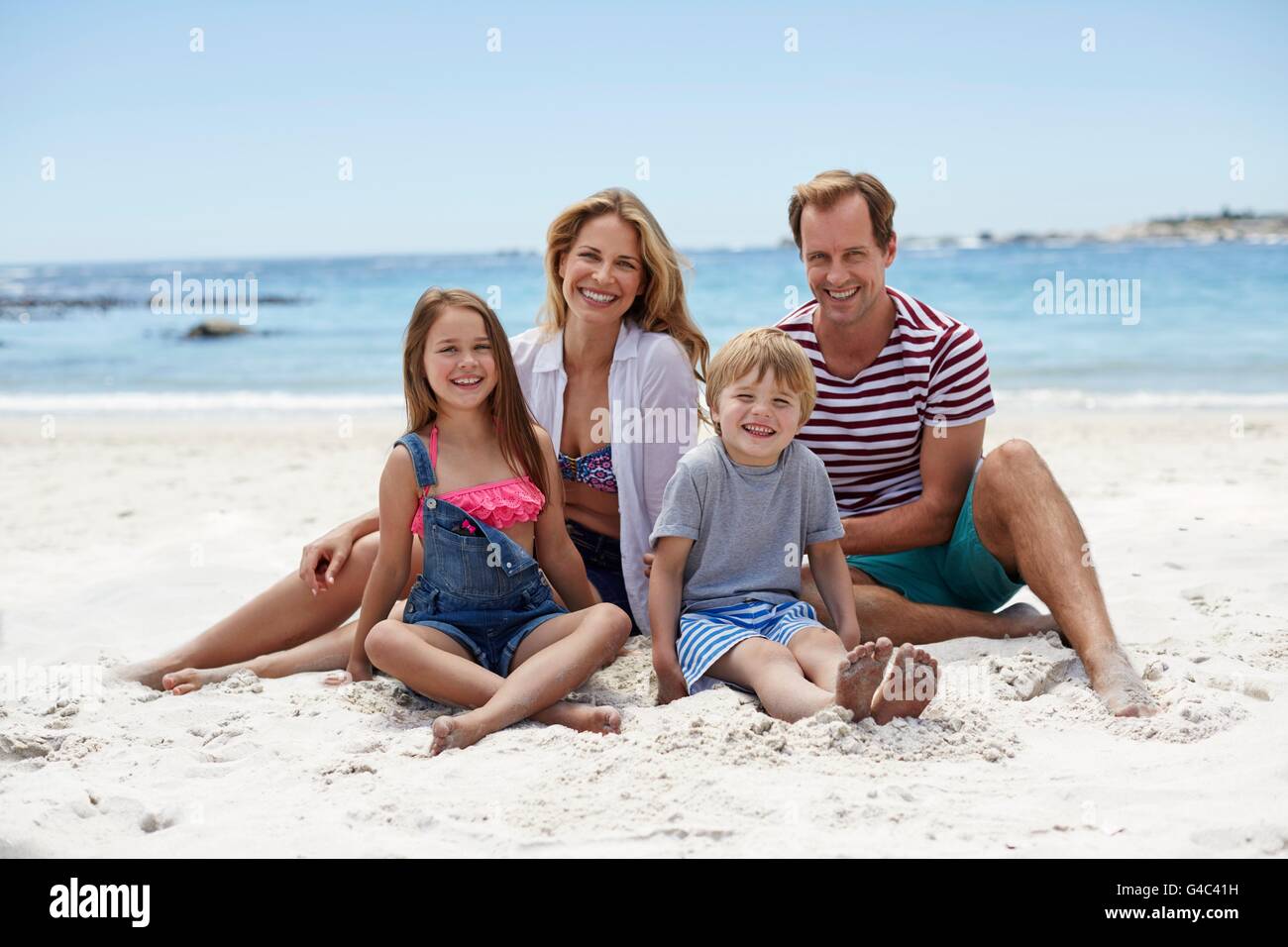 Modello rilasciato. Famiglia con due bambini seduti sulla spiaggia, ritratto. Foto Stock