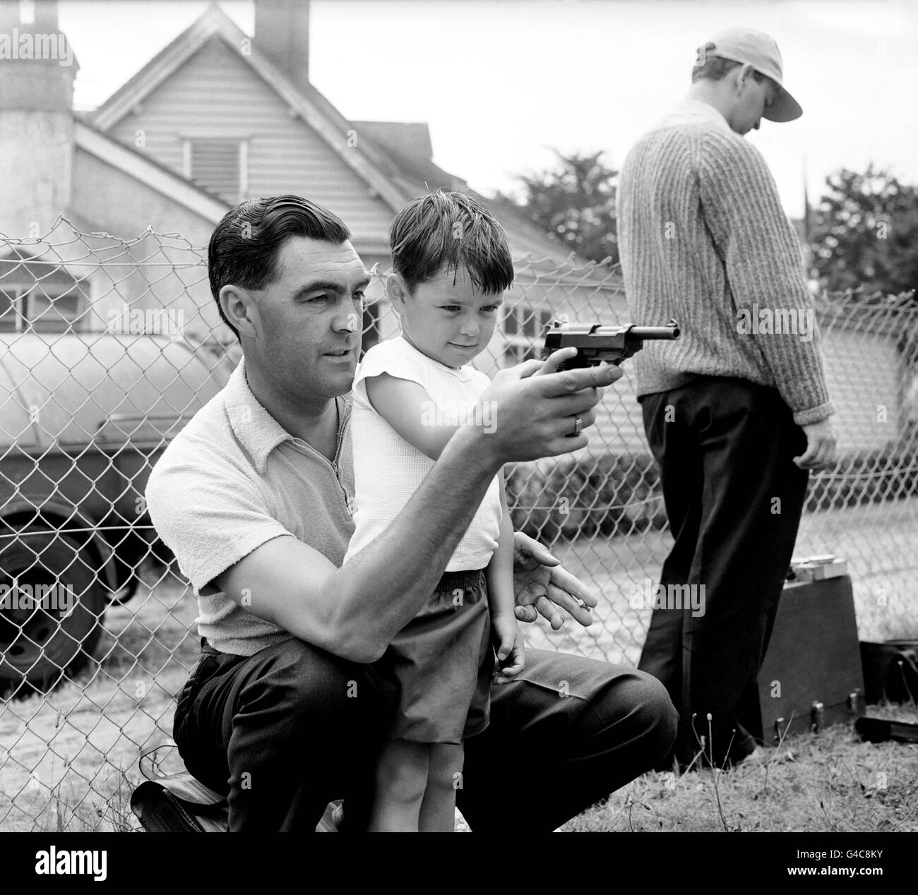 Tiro - Police Force Pistol Shooting Competition - Bisley. Neil Brown di quattro anni è mostrato come tenere una pistola automatica P38 da suo padre P.C. Dennis Brown, un membro della squadra di polizia Surrey. Foto Stock