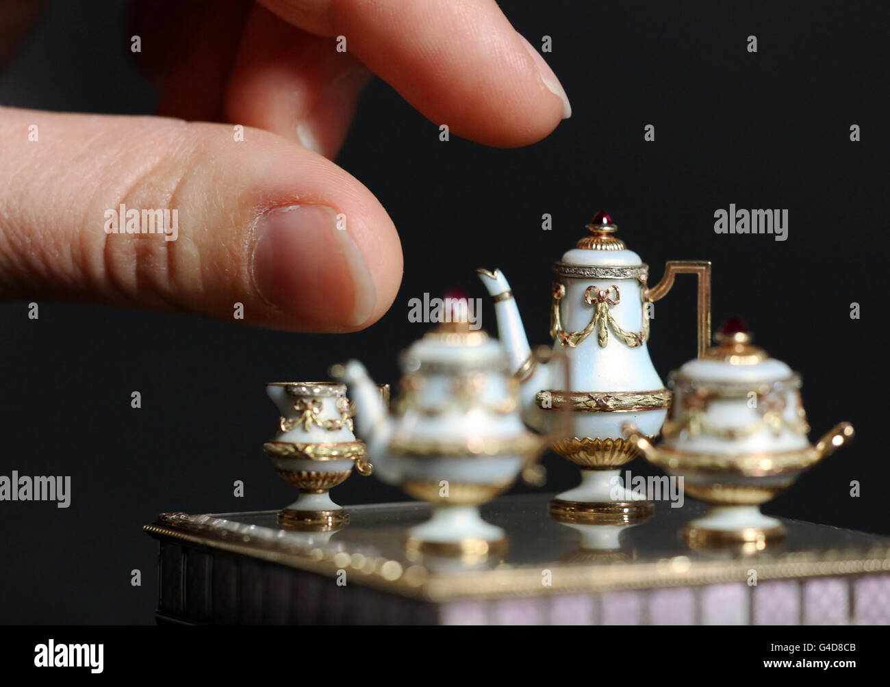 Un curatore della Royal Collection esamina un set da tè in miniatura di 1 cm di altezza, realizzato da un gioielliere russo e orafo Peter Carl Faberge, originariamente di proprietà della regina Alexandra, parte della nuova mostra Faberge a Buckingham Palace, Londra, che ha aperto sabato 23 luglio. Foto Stock