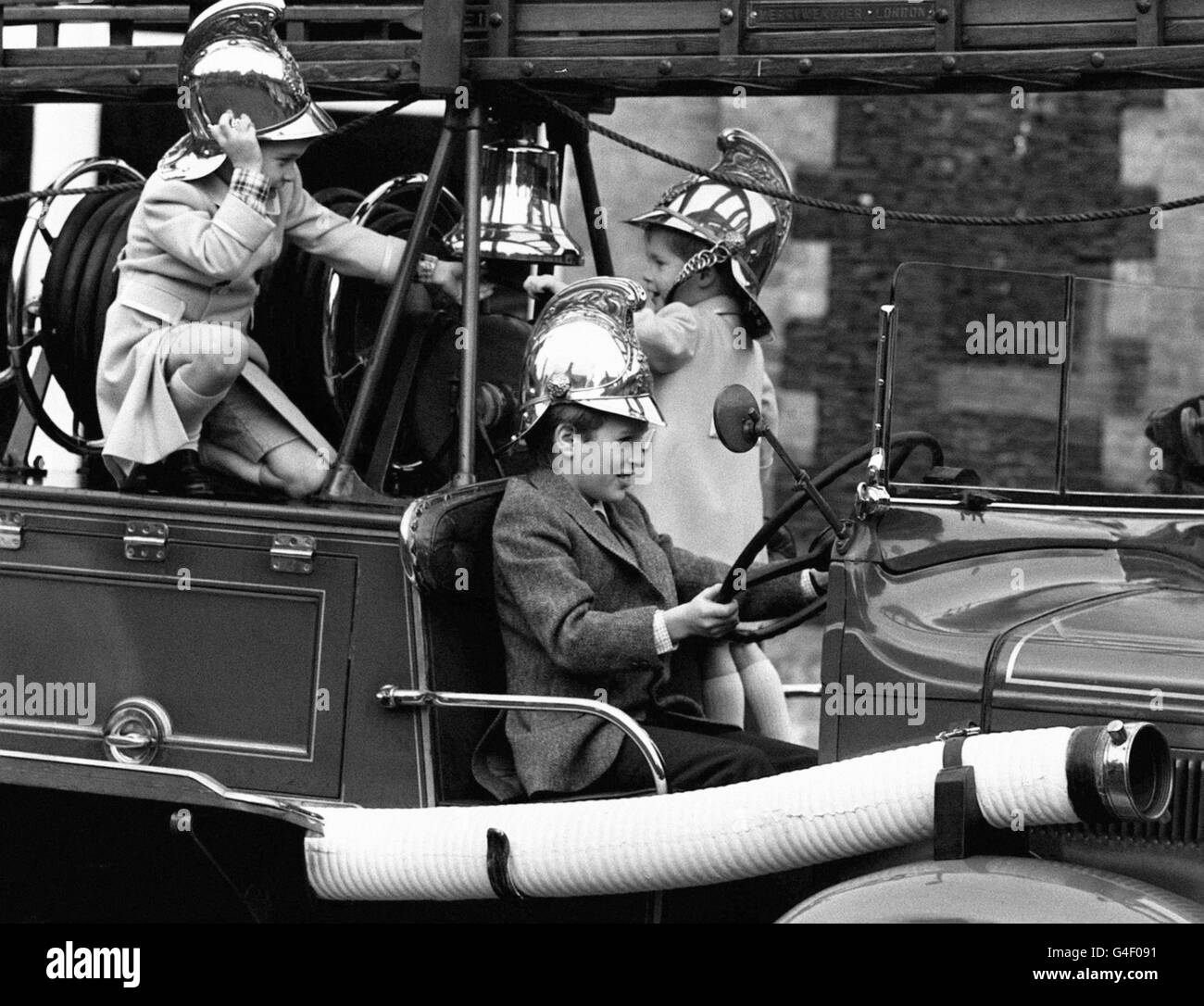 Il principe William , di 5 anni, a sinistra, e il principe Harry, 3, suonano la campana del motore d'annata del fuoco 'Merryweather' con Peter Phillips al volante quando i cugini reali giocarono ad essere vigili del fuoco nel cortile della vecchia stazione dei vigili del fuoco nei terreni della Sandringham House. Foto Stock